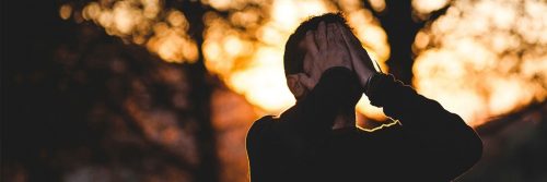 man stands hands in face feeling sad shameful in forest in sunny sky