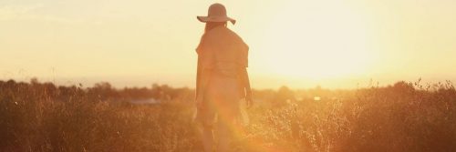 woman facing backward stands on field walking in beautiful sunny sky