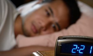 man lies on pink pillow tiredly looking at clock having insomnia problem