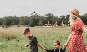 close knit happy family parents with three little adorable kids walking on green field