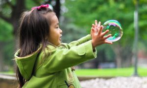 little girl stands in park playing with bubble