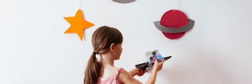 little girl plays toy beside white wall decorated with universe symbols