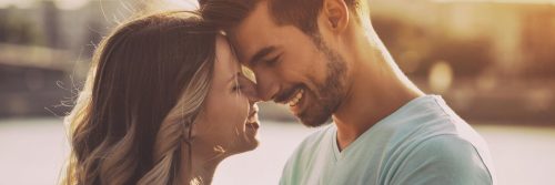 couple stands head to head happily smiling in sunny sky