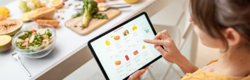 woman shopping online for healthy fruits beside healthy vegetables bowl broccoli on chopping board on table