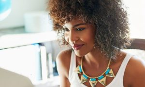 curly hair woman happy face sitting in bright office room small white bookshelf