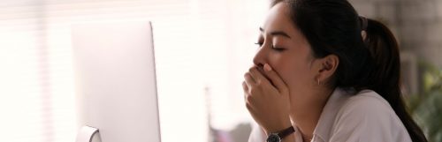 woman hand covering mouth feeling sleepy tired when looking at laptop