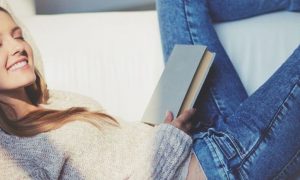 girl eyes closed happily smiling lying on white couch holding book