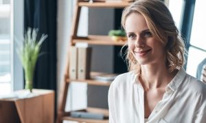 young woman with short blonde hair smiles board wooden drawer side table clothes hanging behind