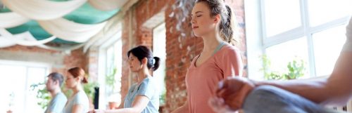 group of woman eyes closes sits leg crossed concentrates on meditation in quiet room