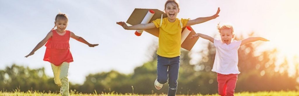 three children happily excitedly running on grass in sunny sky