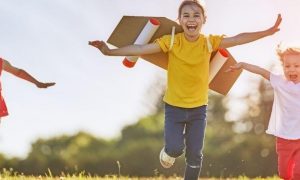 three children happily excitedly running on grass in sunny sky