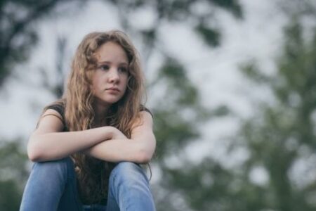 Portrait of young sad teen girl sitting outdoors on the railway at the day time. Concept of sorrow.