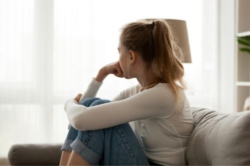 Side view young woman looking away at window sitting on couch at home. Frustrated confused female feels unhappy problem in personal life quarrel break up with boyfriend or unexpected pregnancy concept