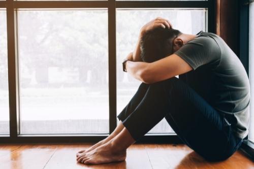 Depressed man. Sad unhappy Man sitting on the floor and holding his forehead while having headache