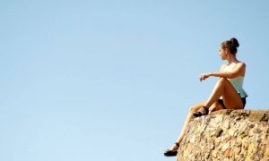 woman sits on rock looking blue clear sky