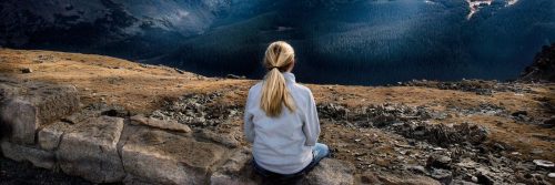 woman sits on rock facing backward focuses on breathing immersing into nature