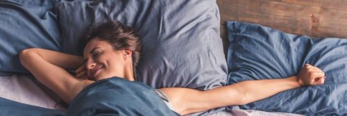 woman wakes up happily smiling stretching up on bed