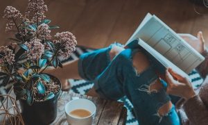 woman sits on floor beside side table tea cup reading book