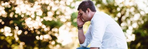 man tiredly sits hand in face thinking in sunny sky