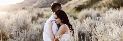 couple stands on field hugging in sunny sky