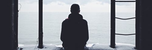 person sits backward facing ocean in cloudy sky