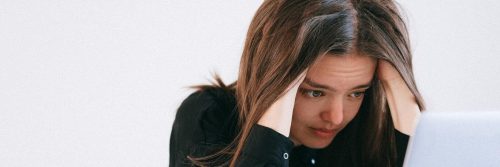 woman hands on face sadly looks at laptop