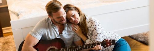 man playing guitar while girlfriend lying on shoulder listening