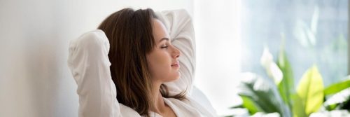 woman eyes closed sits in living room hands over head focusing on inner peace