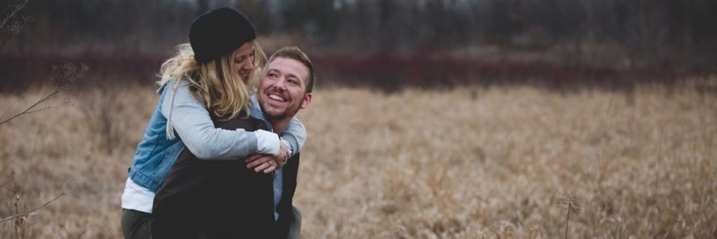 couple happy faces looking smiling in field while man carrying partner