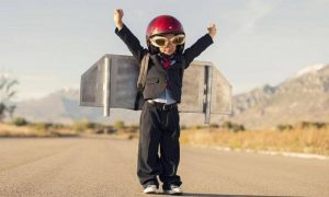 small kid stands alone raising hands carrying airplane designed bag