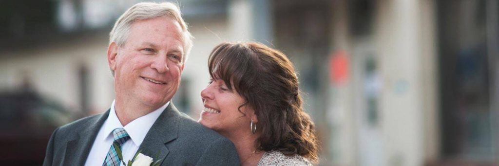 married elderly couple stands on street happily smiling