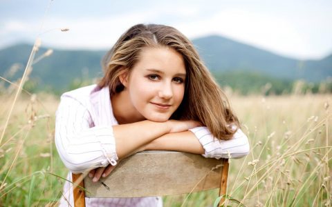 woman sits on chair on field happily smiling posing for photos