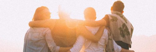 group of close friends stands facing backward hugging each other looking at sunny sky