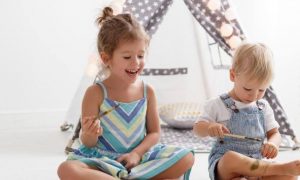 two adorable naughty children sits in living room painting on hands beside toys teddy bear