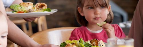 little adorable girl sits beside healthy vegetable dishes eating vegetable cucumber