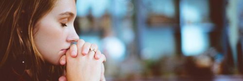 woman eyes closed sits holding hands thinking praying