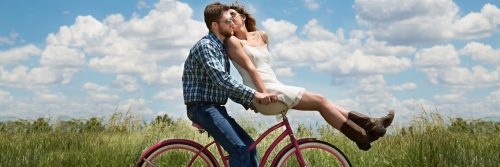 couple happily ride along green field while woman sits in front kissing partner