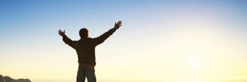 man stands alone raising hands feeling grateful about life in sunny blue sky