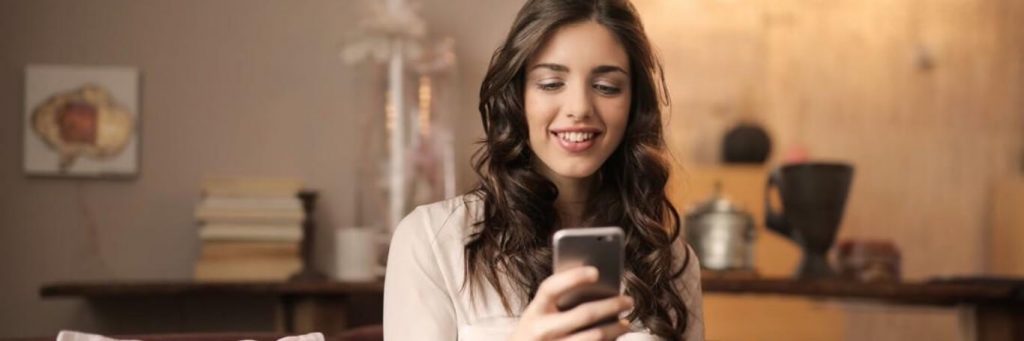 woman happily smiles using mobile phone in tidy living room