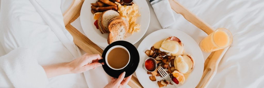 two breakfast dishes on bed drinks coffee juice