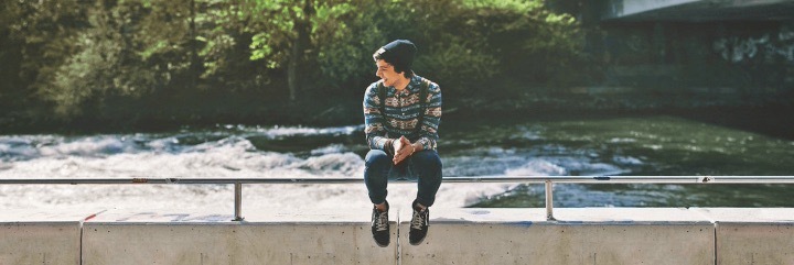 man sits on cliff beside ocean happily smiling