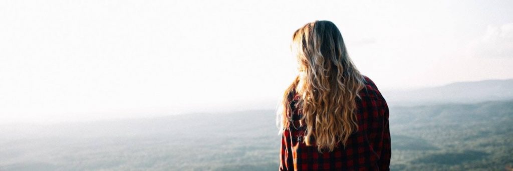 woman facing backward stands looking at sunny sky in foggy weather