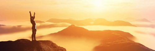 person stood on top of mountain raises hand gratitude life in beautiful foggy sunny weather