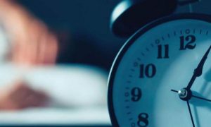 black clock next to bed man struggling to sleep at night