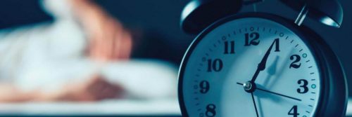 black clock next to bed man struggling to sleep at night