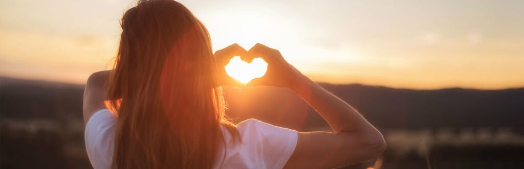 Woman facing the golden sunset making a love heart shape