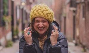 excited woman with yellow beanie and dark blue winter coat stands alone between two arrays of buildings