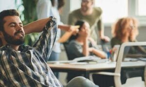 man hands over head sits in office focuses on personal computer