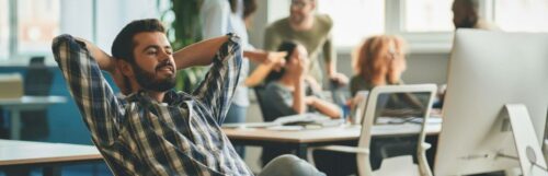 man hands over head sits in office focuses on personal computer