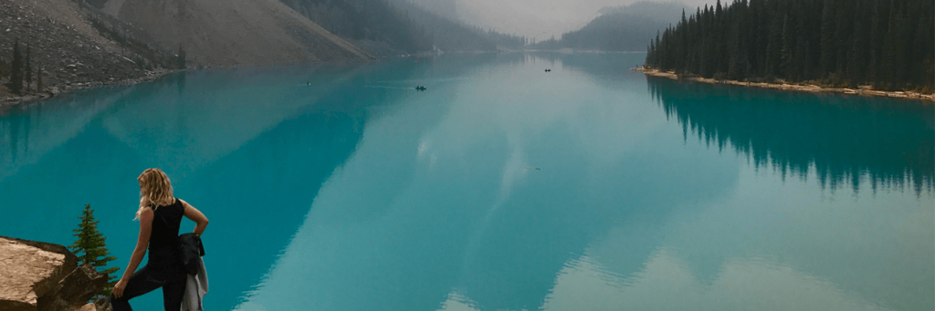 woman stands on rock beside blue ocean mountain forest foggy weather